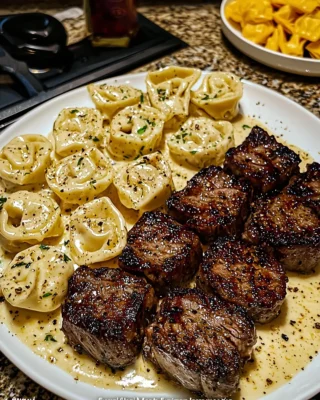 Garlic butter steak bites served with creamy pesto Alfredo tortellini on a white plate