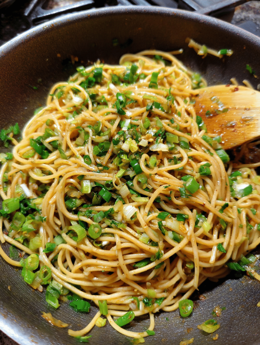 Close-up of ginger scallion noodles in a bowl, topped with sliced scallions and sesame seeds, served as a quick Asian-inspired meal.